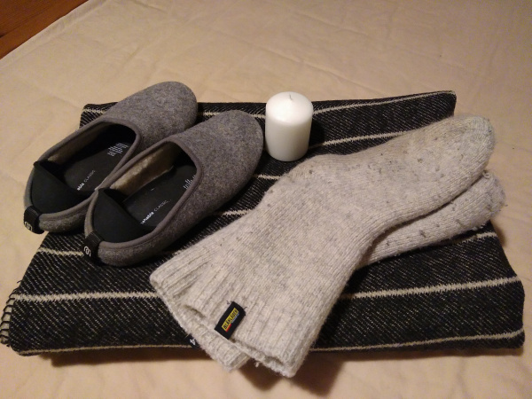 Pictured are socks, slippers, and a blanket, all made out of thick wool, as well as a candle.